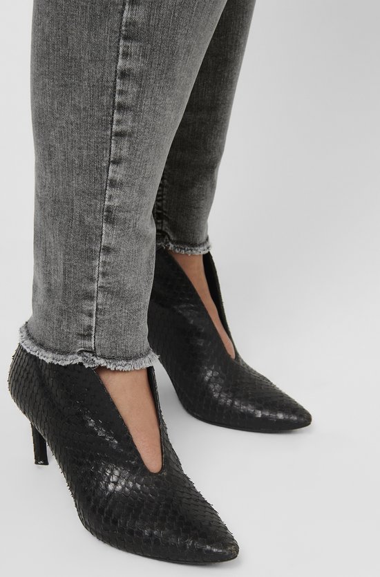 Close-up van grijze skinny jeans met rafelige zoom en zwarte puntige laarzen met slangenprint.