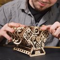 Man met een grijze trui bouwt aan een houten V8-motor model, waarbij hij de details vastpakt.