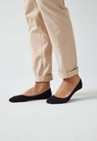 Voetjes in zwart, gedragen met een beige pantalon met omgeslagen pijpen.