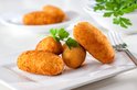 Vier goudbruine kroketten en één ronde bitterbal op een wit bord, gegarneerd met peterselie.
