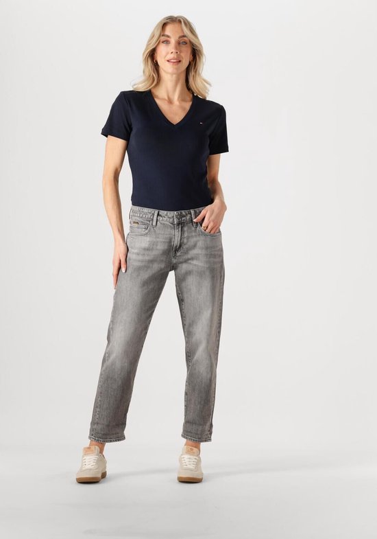 Model draagt een grijze jeans met opgerolde broekspijpen en beige sneakers.