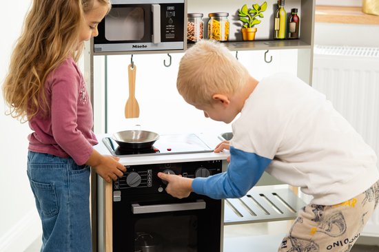 Kinderen spelen met een speelkeuken. Jongen plaatst potje in magnetron, meisje kookt.