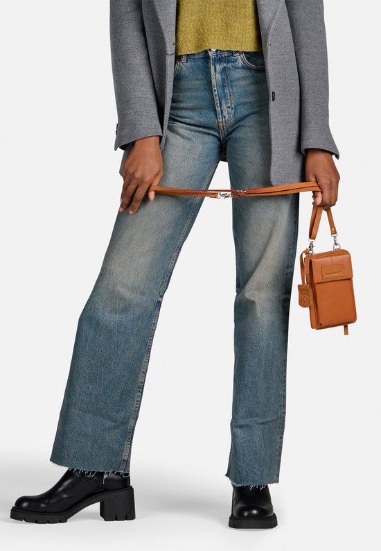 Model met cognac gekleurde telefoonportemonnee aan een lange schouderband, met spijkerbroek en blazer.