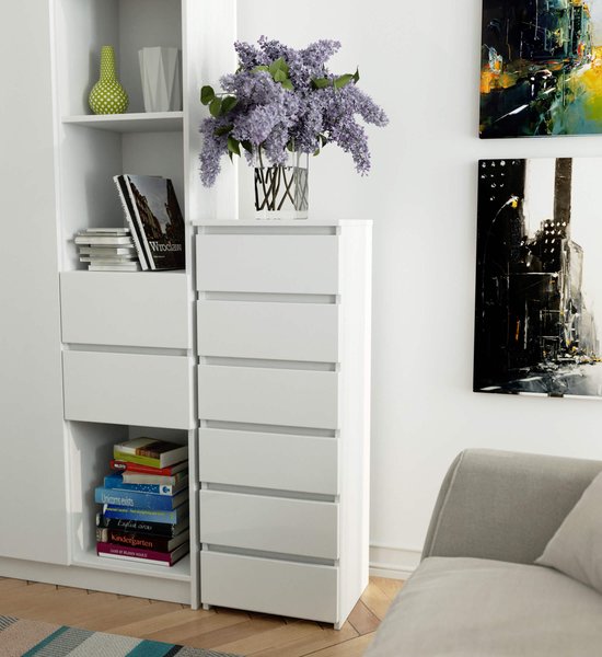 Witte ladekast met zeven lades naast een witte boekenkast met boeken en decoratie.
