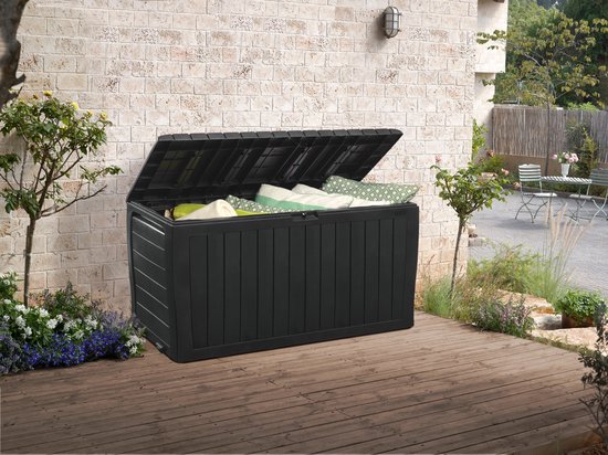 Zwarte opbergbox met open deksel, gevuld met kussens, in een tuin met houten vlonder.