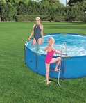 Meisje in roze badpak op een zwembadladder in een ronde blauwe zwembad, met een vrouw in een donker badpak.