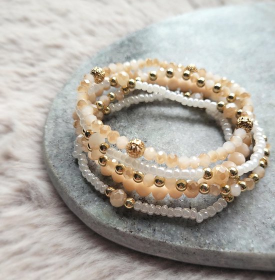 Set van vijf armbanden met roze, crèmekleurige en witte kralen en gouden accenten op een grijze steen.
