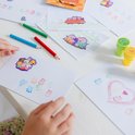 Een kind drukt Peppa Pig stempels op papier, met potloden en stempels op de tafel.