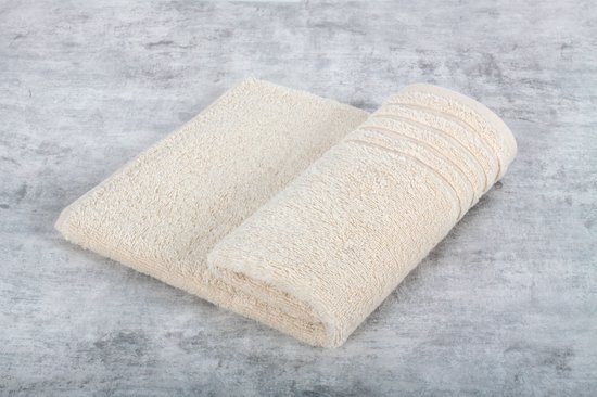 Een opgerolde, crèmekleurige handdoek met ribbels aan de rand, op een grijze ondergrond.