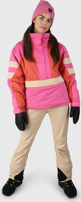 Model in een roze en oranje ski-jas met beige strepen en een roze muts. Ze draagt een beige skibroek en zwarte handschoenen.