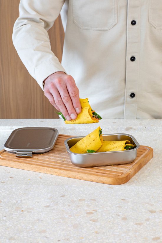 Torse d'une personne plaçant des wraps dans une boîte à lunch en inox.