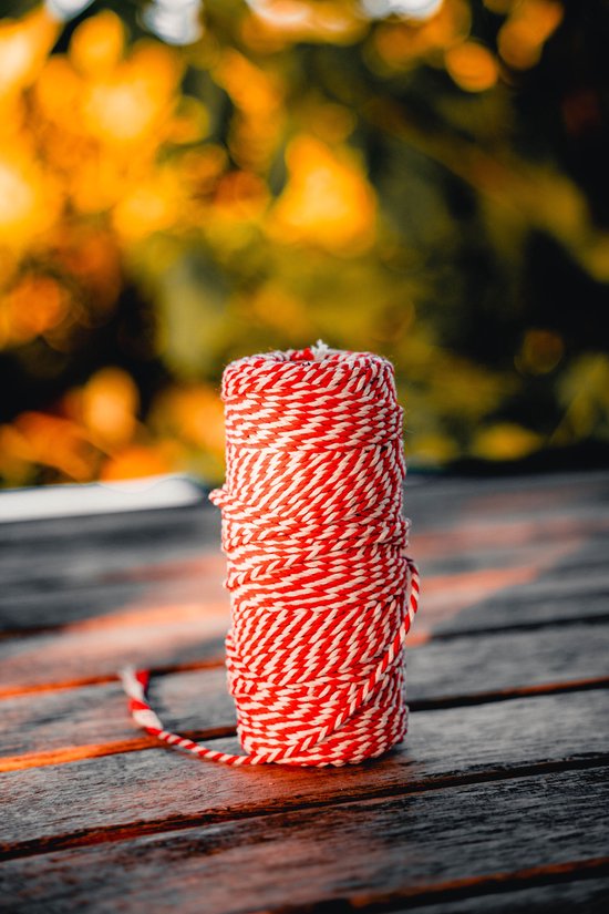 Een rol rood met wit gevlochten keukentouw op een houten ondergrond, met zachte achtergrond.