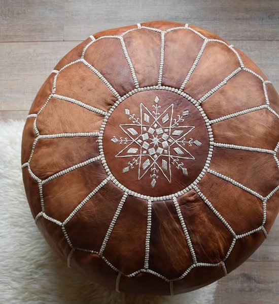Een cognacbruine lederen poef met een rond wit sterenpatroon in het midden, op een houten vloer.