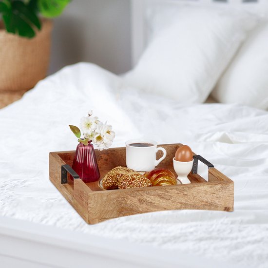 Houten dienblad met croissants, koffie, een gekookt ei en bloemen, op een bed.