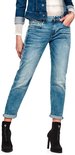 Gedragen voorkant van een vrouw in een lichte, gescheurde jeans met opgerolde broekspijpen en zwarte laarzen.
