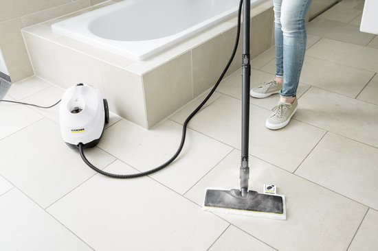 Femme utilisant un nettoyeur vapeur sur un sol carrelé clair près d'une baignoire.