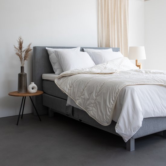 Wit, gewatteerd dekbed op een opgemaakt bed met witte lakens. Het dekbed heeft een licht crème kleur.