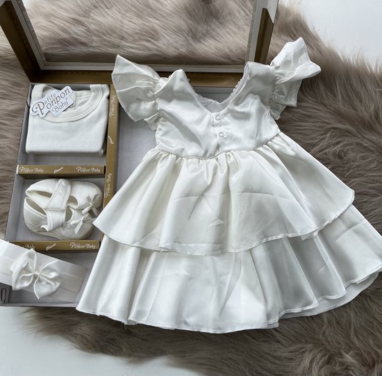 Babyjurk in ivoorkleur met ruches, parelmoeren knopen op de rug en gelaagde rok. Bijpassende haarband en schoentjes.