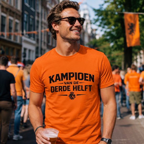 Oranje T-shirt met tekst "KAMPIOEN VAN DE DERDE HELFT" en een leeuwenlogo, gedragen door een man met zonnebril.