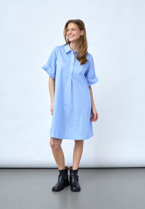 Une robe bleu clair à rayures verticales blanches, avec des manches courtes intégrées et un col. Portée par un mannequin avec des bottines noires.