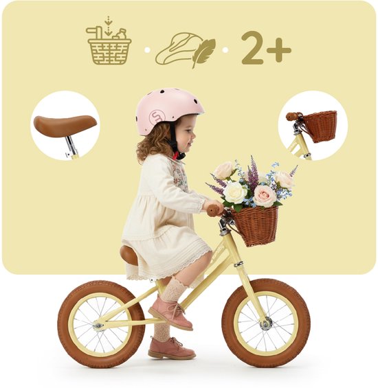 Meisje met roze helm en jurk zit op gele loopfiets met bloemenmandje. Ze draagt roze schoenen en kousen.