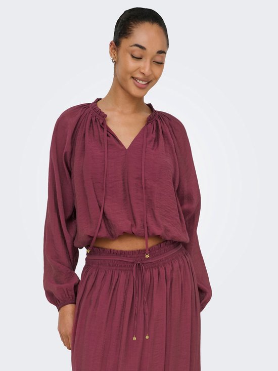 Model draagt een bordeauxrode crop top met pofmouwen en een v-hals met strikdetail.
