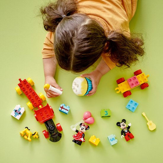 Meisje speelt met LEGO DUPLO Mickey & Minnie verjaardagstrein onderdelen: Mickey, Minnie, Pluto, een gitaar, cadeautjes en blokken met getallen.