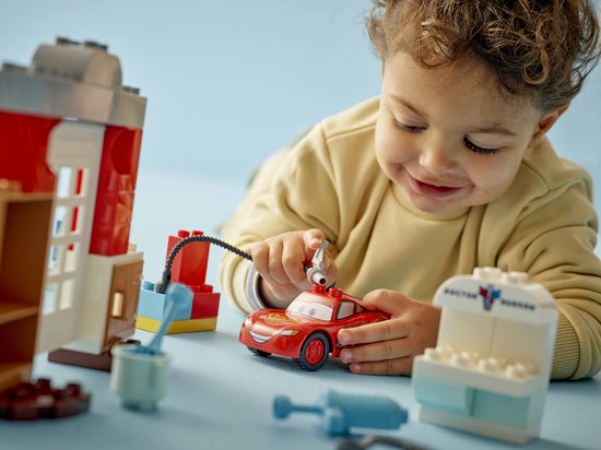Jongetje speelt met rode LEGO Duplo Lightning McQueen auto en de doktersgarage. Sluit de slang aan op de auto.