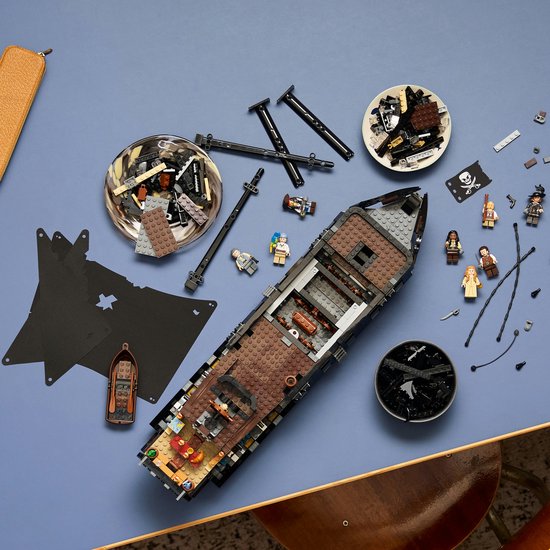 Un modèle LEGO du navire pirate du Capitaine Jack Sparrow avec des voiles noires et des figurines sur un fond bleu.