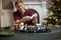 Vrouw bouwt aan een blauwe LEGO-trein met kerstdecoraties, met op de achtergrond een kerstboom.