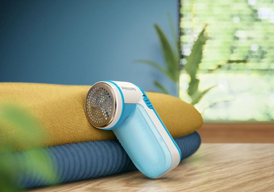 Lichtblauwe Philips pluizenverwijderaar met witte accenten, liggend op een stapel kleding.