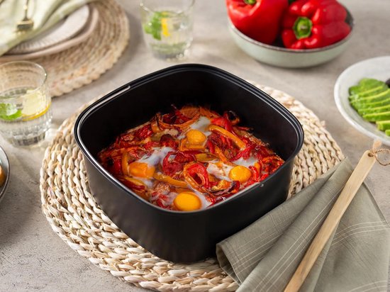 Airfryer met een ovenschotel gevuld met eieren, paprika's en uien.