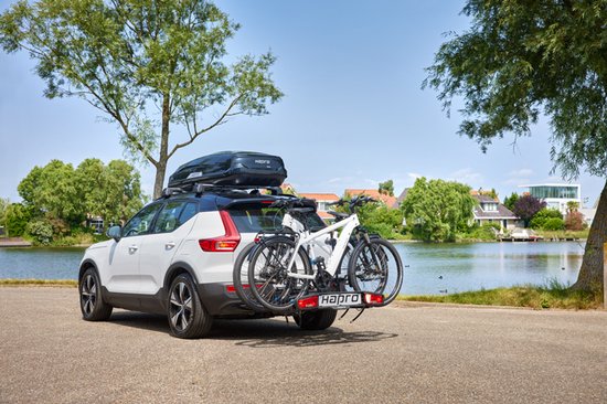Witte auto met dakdragers en een fietsendrager met twee fietsen, staande aan de oever van een meer.