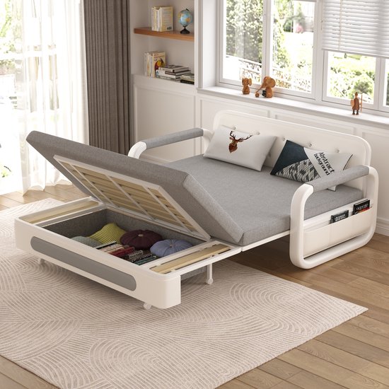 Grijze sofa met open klapzitting, opbergruimte vol met kussens.
