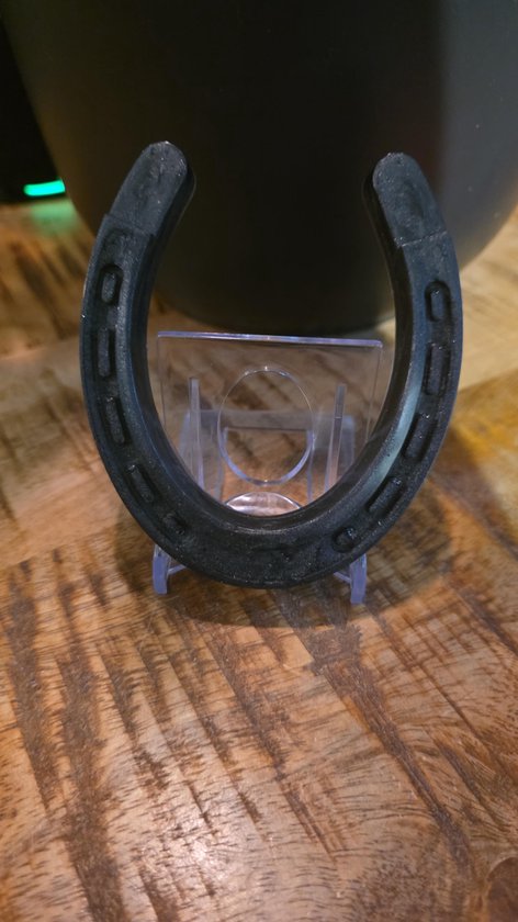 Zwart metalen hoefijzer met duidelijke groeven, geplaatst op een transparante houder.