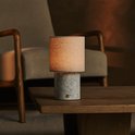 Een marmeren tafellamp met een beige linnen kap staat op een houten tafel.
