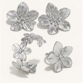 Zilverkleurige oorbellen, ring en armband in bloemvorm op witte achtergrond.