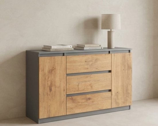 Dressoir met antracietkleurige zijkanten en een Lancelot eikenhouten voorpaneel met drie laden. Staat op een tafel met boeken en een lamp.