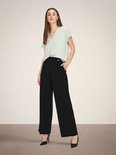 Model draagt zwarte wijde broek met hoge taille en een lichtgroen shirt.