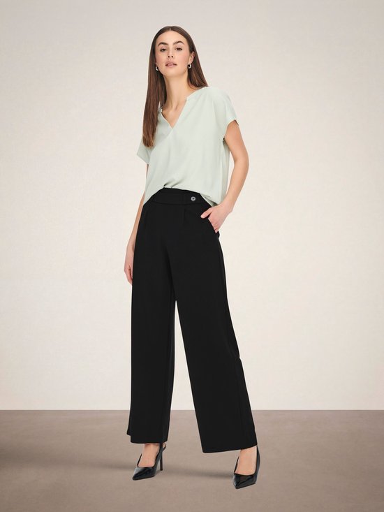 Model draagt zwarte wijde broek met hoge taille en een lichtgroen shirt.