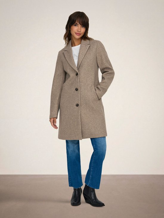 Model in bruine jas, witte top en blauwe jeans.