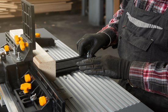 Handen met zwarte handschoenen stellen een zwarte geleiderail in op een grijze tafel met ribbels.
