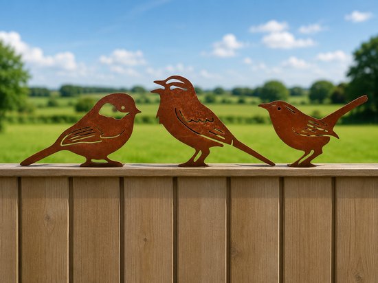 Trois oiseaux métalliques couleur rouille sur une clôture en bois, avec un fond vert et un ciel bleu.