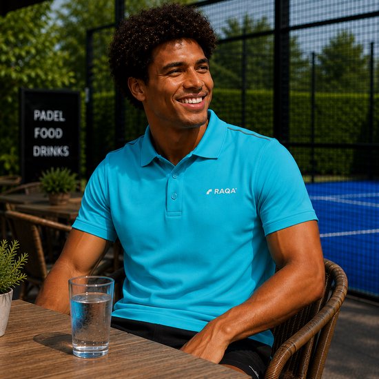 Man met krullend haar zit aan tafel, draagt hemelsblauwe Raqa polo, met glas water.