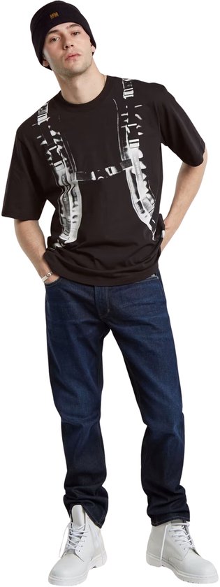 Man met donkerblauwe G-Star Mosa Straight jeans, zwart T-shirt met print, zwarte muts en witte laarzen.