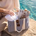 Close-up van blauw-wit gestreepte strandtas met tijdschrift, fles en zonnebril.