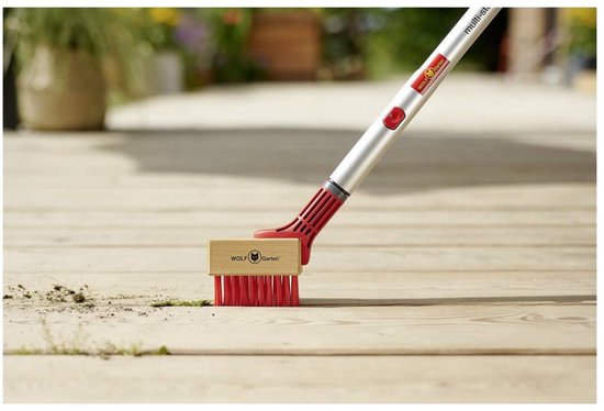 Voegenschraper met houten kop en rode borstelharen veegt vuil van houten terras.