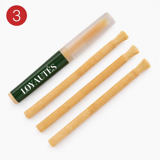 Drie miswak stokjes met een groen-gouden houder van Loyautés met het opschrift 'LOYAUTÉS'.