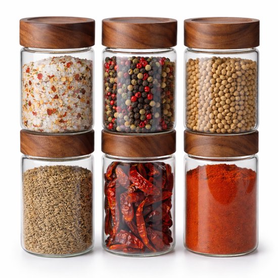 Six pots de stockage en verre avec couvercles en bois, remplis de flocons de sel, grains de poivre, soja, cumin, piments séchés et poudre de paprika.
