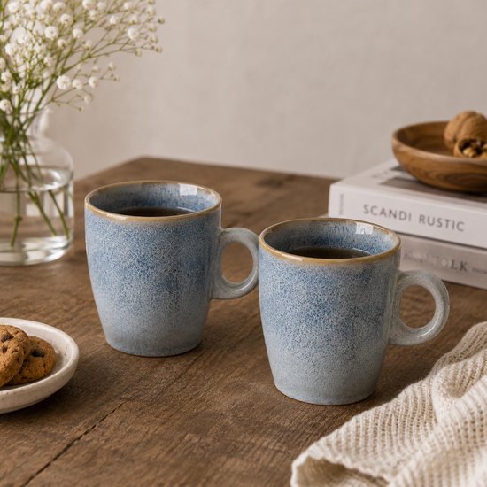 Twee lichtblauwe mokken met handvat, gevuld met koffie, op een houten tafel.
